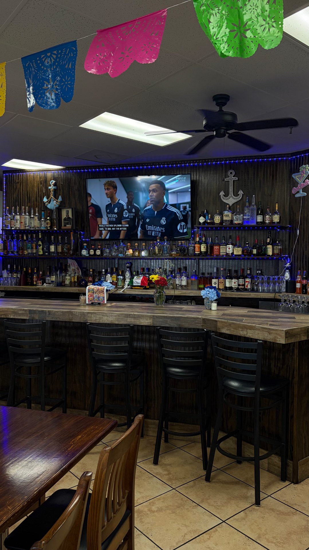 The full bar at La Palapa Mariscos Bar with bar stools and TVs.